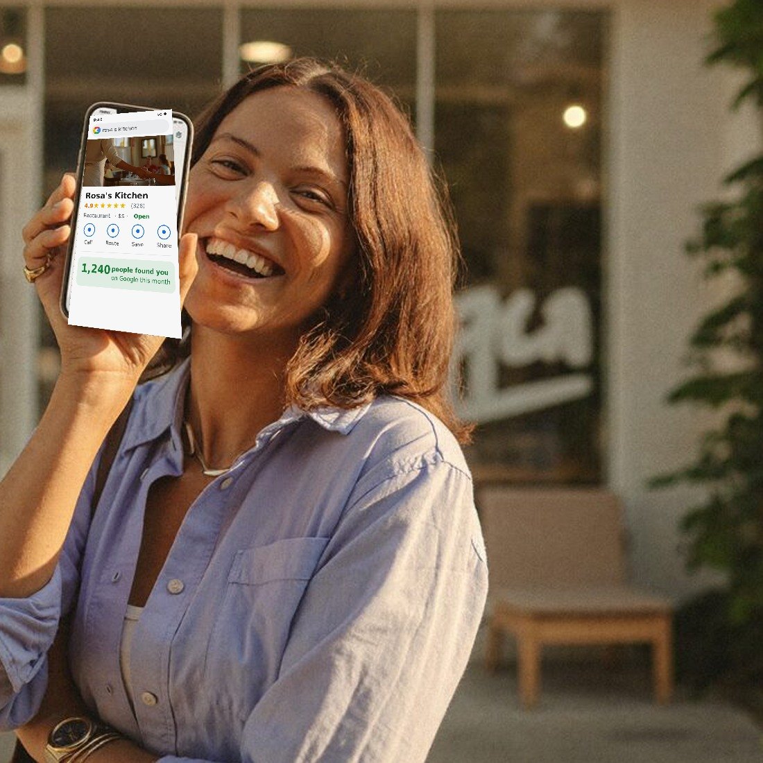 A proud local shop owner holding their phone showing their business page in front of their store